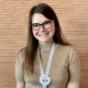 Headshot of Christine Kelly smiling in a brown sweater with a lanyard with a Chelsea's Hope #FightLafora pin.