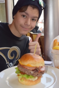 Mathys Lucas smiling and holding a thumbs up behind a burger.