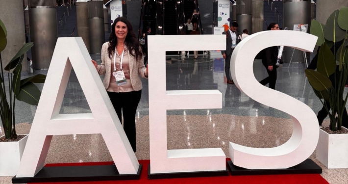 Jenifer smiling behind an AES sign