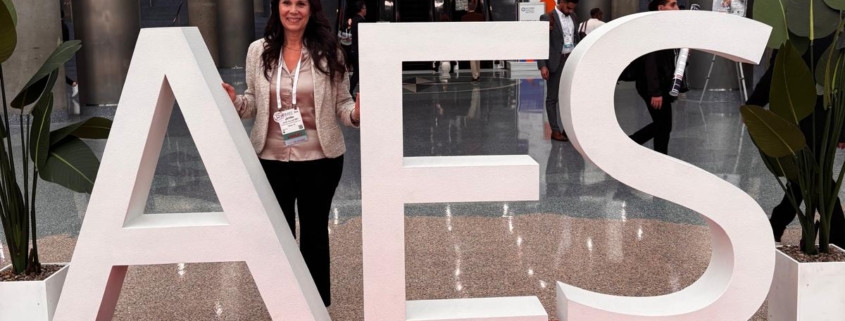 Jenifer smiling behind an AES sign